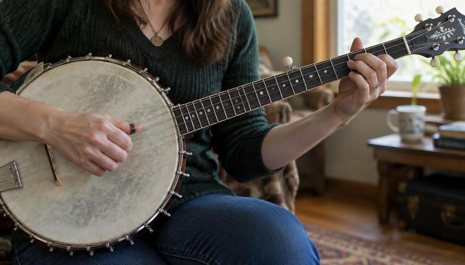 Close-up of an adult playing a five-string open-back banjo in natural light